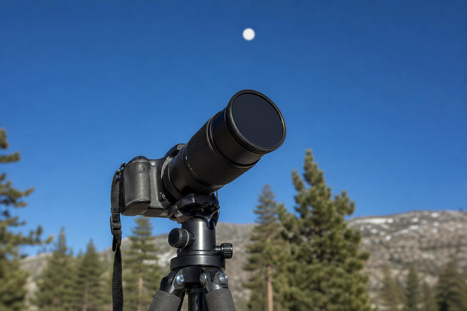 A DSLR on a tripod with a solar filter mounted on the front of the lens, aimed at the Sun in a clear daytime sky.