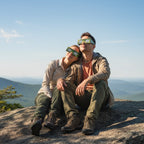 A young couple wearing Army design eclipse glasses on a rock, sharing a moment of awe, enjoying the outdoors.