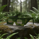 A professional still life of Army design eclipse glasses on a mossy stone in a green forest, ISO 12312-2 compliant.