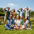 A group of friends wearing Bloom solar eclipse glasses at a vibrant party, sharing joyful moments under the sun in a lush backyard. ISO 12312-2 certified.