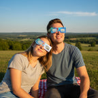A young couple sharing an intimate moment in a sunny park, wearing Breeze design eclipse glasses while looking at the sky. Perfect for August 12, 2026.
