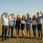 A diverse group of colleagues wearing Bull design glasses, looking up in awe during a team-building event on a sunny ranch.