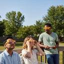 Tres amigos disfrutando de una reunión soleada en una terraza, con gafas diseño Bull, a la espera del eclipse del 12 de agosto de 2026.