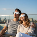 Couple élégant portant des lunettes design Cipher sur un patio de toit, partageant l'émerveillement en regardant le ciel, sûres pour l'éclipse du 12 août 2026.