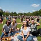 A diverse crowd enjoying a public event, all wearing Coldsoup eclipse glasses while looking up, celebrating together.