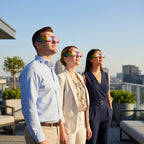 Professionals at a corporate event wearing Colorsplash glasses, looking up in awe under midday sun.