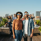 A vibrant rooftop gathering with friends wearing crowd design solar eclipse glasses, sharing awe and joy under a clear blue sky.
