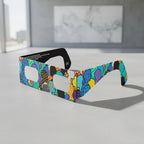 A professional still life shot of crowd design solar eclipse glasses on a textured, light grey surface. ISO 12312-2 compliant.