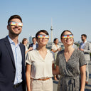Compañeros en Berlín disfrutando de un evento de empresa, todos con gafas diseño DE mirando al cielo con asombro ante el eclipse del 12 de agosto de 2026.