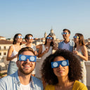 Amigos elegantes en una fiesta en la azotea de una ciudad europea, todos con gafas diseño EU y mirando al cielo.