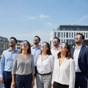 Profesionales en un evento corporativo en una terraza, con gafas diseño EU, mirando al cielo luminoso.