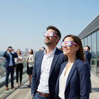 Colleagues on a rooftop terrace in London, wearing GB eclipse glasses while looking up. Enjoy a safe viewing experience on August 12, 2026.