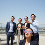 Four colleagues on a rooftop terrace looking at the sky while wearing Goo design glasses, sharing a moment of excitement.