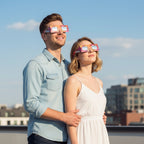 A stylish couple wearing graffiti design eclipse glasses on a city rooftop, sharing a moment of wonder while looking up at the sky.