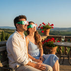 A couple on a Tuscan terrace, wearing IT design solar eclipse glasses, gazing up in quiet awe together.
