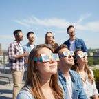 At a rooftop party, friends wearing Memphis design eclipse glasses gaze upward in wonder, meeting EN 166 standards.