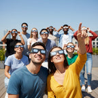 A group of friends at a rooftop party, wearing Music design glasses and gazing upwards with expressions of wonder. CE certified eclipse viewers.
