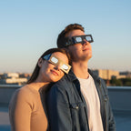 A stylish couple on a rooftop terrace, both wearing Music design solar eclipse glasses, sharing a moment of awe. Perfect for August 12, 2026.
