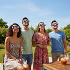 Four friends wearing bright neon eclipse glasses on a sunny patio, sharing wonder as they look at the clear blue sky.