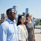 Three professionals standing on a rooftop, wearing Orbiter glasses and looking up in wonder at the sunny sky.