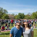 A large group at a community event, wearing solar eclipse glasses and looking up at the sky, creating a joyful atmosphere. August 12, 2026.