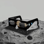 Solar eclipse glasses resting on a dark grey slate rock surface, evoking a cosmic theme. ISO 12312-2 certified.