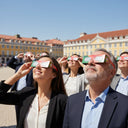 Diverse group enjoying a corporate event in a European square, all wearing eclipse glasses and focused on the sky.