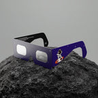 Solar eclipse glasses resting on a textured rock surface, showcasing ISO 12312-2 certified design.