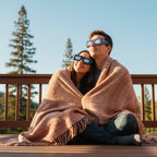 A couple shares a cozy moment wearing Stranded design eclipse glasses on a wooden deck, gazing at the sky together. Perfect for the August 12, 2026 eclipse.