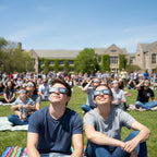 Large crowd on a university campus, with individuals in Swing design glasses looking up at the sky during a public viewing event.