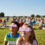 School children and teachers gather on a sunny lawn, all wearing unicorn eclipse glasses, sharing a moment of wonder. Safe for August 12, 2026.