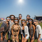 Festival-goers wearing urban eclipse glasses, gazing at the sky in awe during a sunny outdoor event. ISO certified for safety.