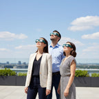 Colleagues at a tech event wearing Voltage solar eclipse glasses, gazing up at the bright sky with curiosity and safety.