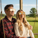 Romantic couple on a wooden porch swing, both wearing Wood design glasses, looking up at the sky with awe. CE certified solar viewers.
